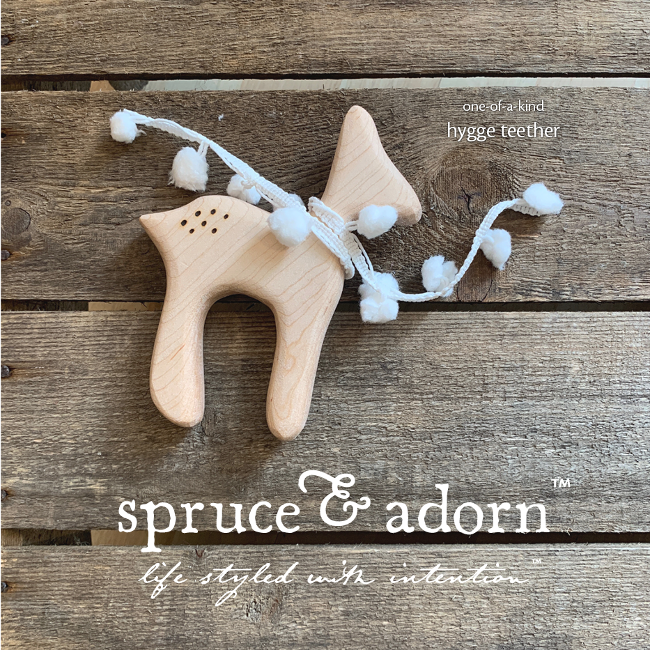 organic, one-of-a-kind, wooden deer shaped teether with cotton ball scarf overlying a wooden background with store logo