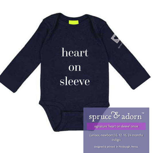 periwinkle description box, overlying indigo colored signature ‘heart on sleeve’ long sleeve onsie reading : signature ‘heart on sleeve’ onsie (unisex • newborn) 12, 16, 18, 24 months with our logo, indigo, designed & printed in Pittsburgh, Pa and a heart on the left arm sleeve